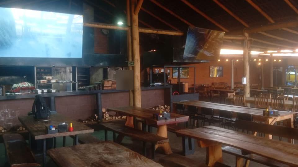 Salão do Costela Brasília, com as mesas de madeira e a churrasqueira ao fundo